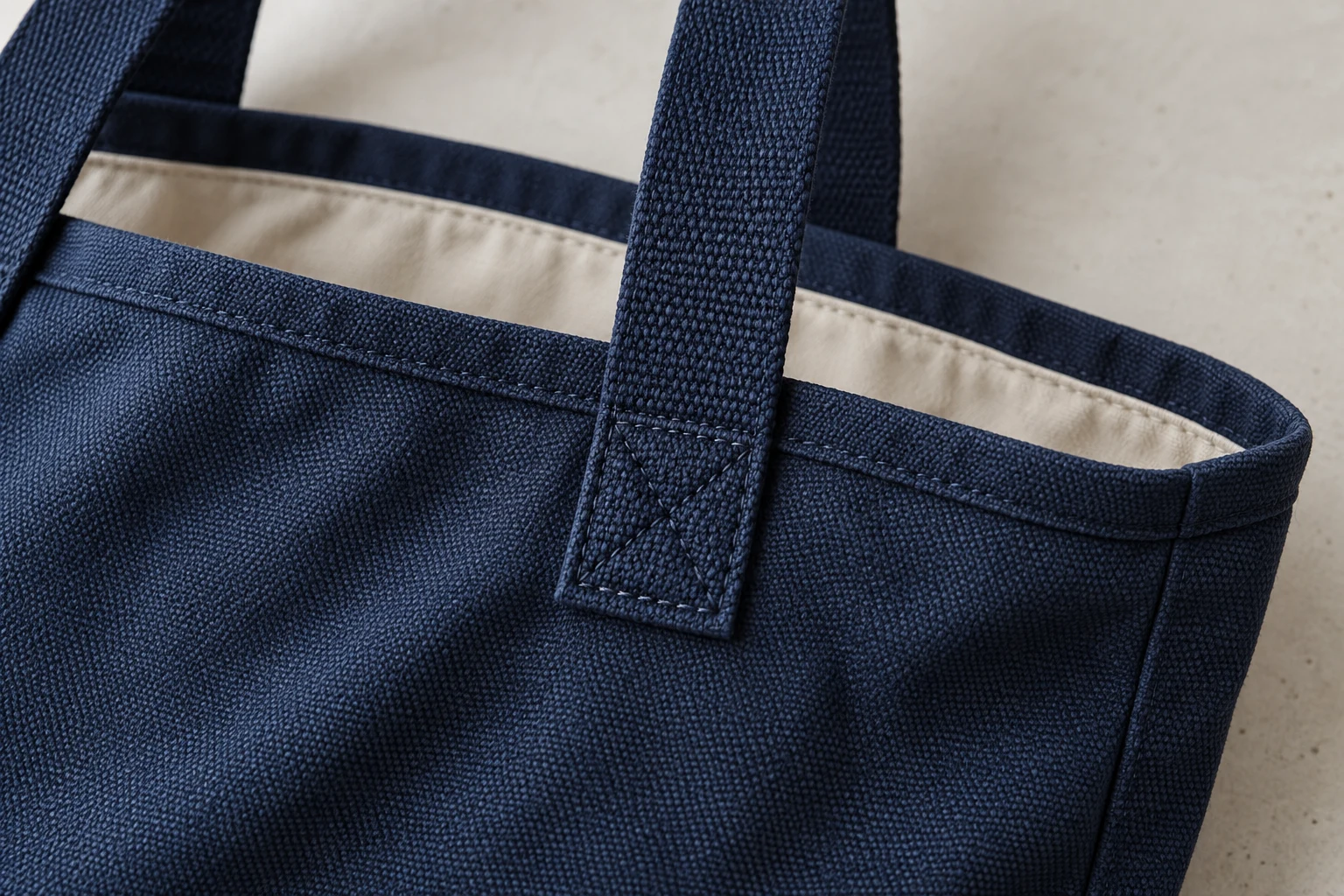 Close-up of navy tote handle reinforcement stitching, bound edge and beige lining