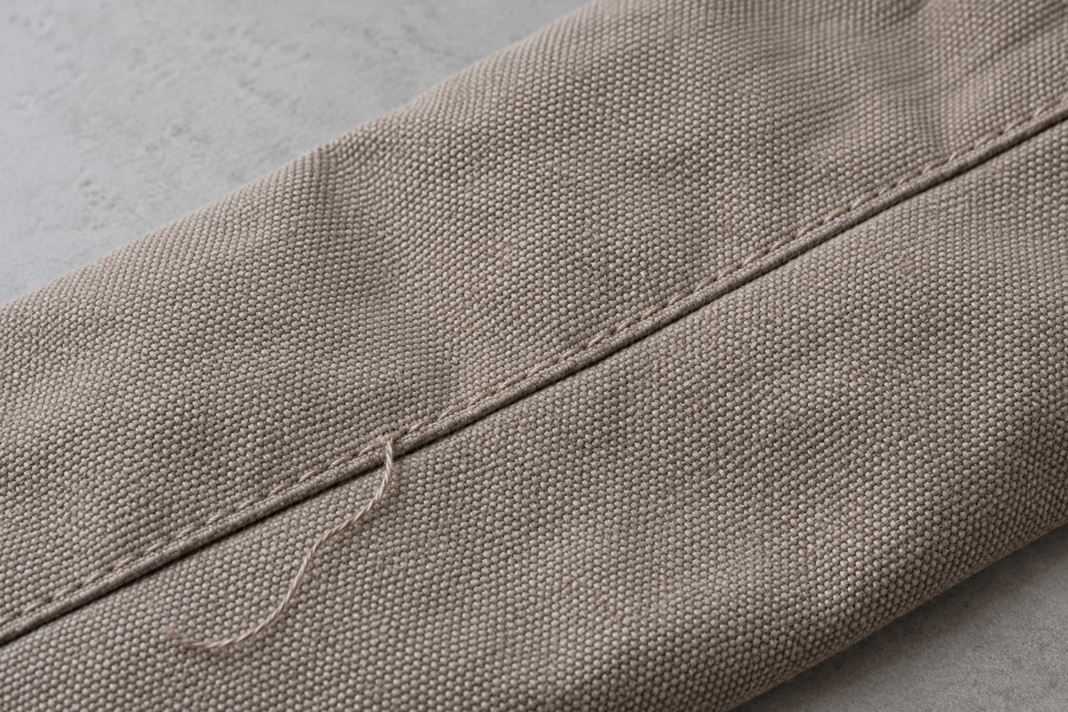 Close-up of a taupe fabric seam with regular stitching and one loose thread tail