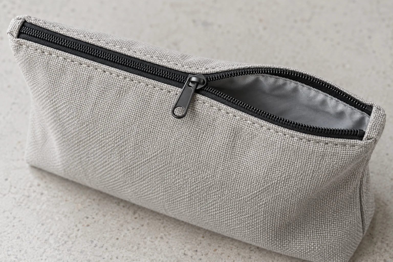 Partly open black zipper on a grey canvas pouch, showing the slider, stitching and recessed lining.